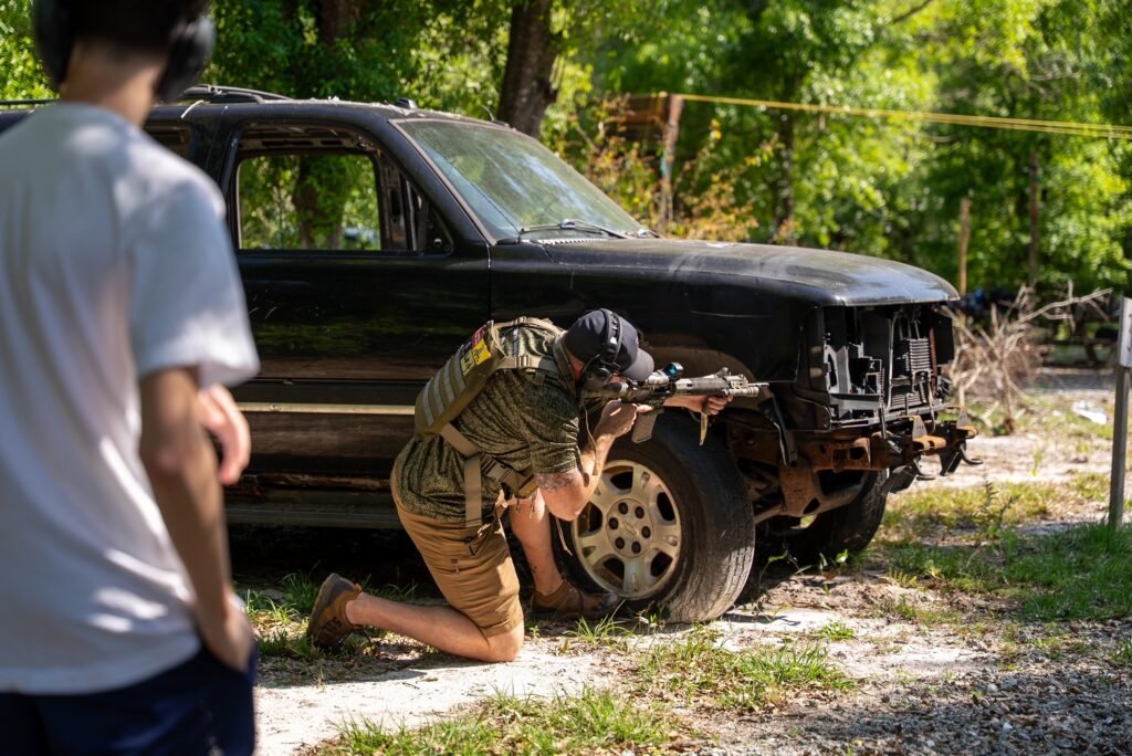 Student shooting from kneeling cover beside a vehicle